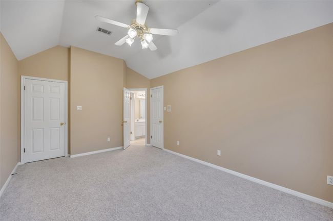 Unfurnished bedroom featuring vaulted ceiling, light carpet, ensuite bathroom, and ceiling fan | Image 32