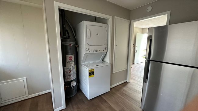 Laundry area featuring water heater, stacked washer and clothes dryer, wood finished floors, and laundry area | Image 6