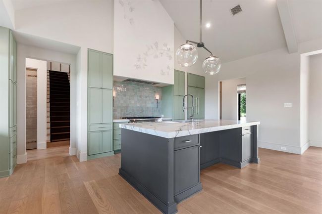 The large island is perfect for entertaining or casual dining. With a knee space for stools, this view is sure to become a familiar one. The range hood has been treated with an artisan-created plaster leaf motif that complements the space. A Thermador 48" professional range anchors the wall beneath. On the right is a 42" fully integrated Thermador French door refrigerator/freezer. The passage on the left leads to the guest suite, powder room, laundry room and garage. | Image 9