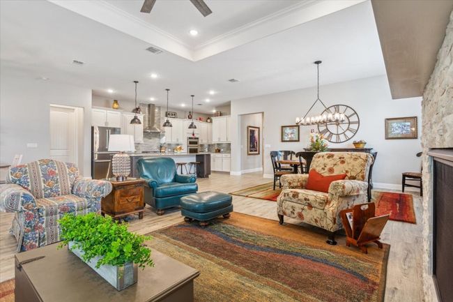 Living area featuring light wood-style tile floors, a chandelier, a ceiling fan, crown molding, and a raised ceiling | Image 11