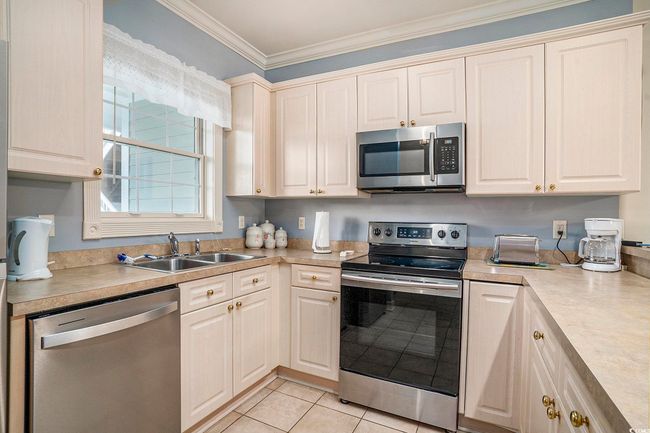 Kitchen with appliances with stainless steel finishes, a sink, ornamental molding, light countertops, and light tile patterned floors | Image 7