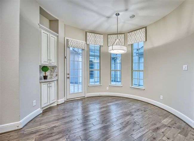 This space features a bright, curved nook with large windows and a glass door, providing ample natural light. It has elegant hardwood floors and a modern light fixture, with built-in cabinetry adding functionality and charm. | Image 24