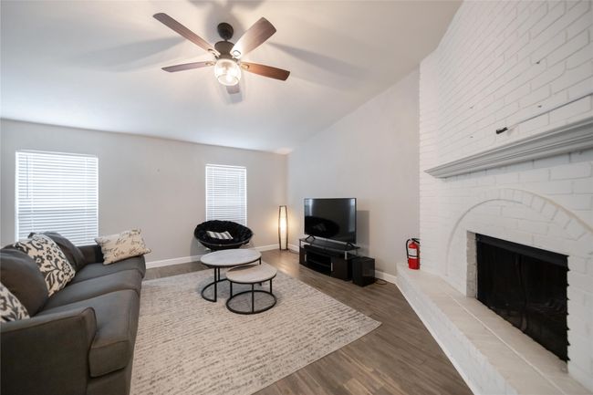 Living area featuring a ceiling fan, wood finished floors, lofted ceiling, plenty of natural light, and a fireplace | Image 4