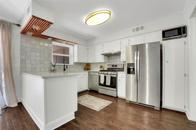 Kitchen with appliances with stainless steel finishes, under cabinet range hood, light countertops, dark wood finished floors, and backsplash | Image 8