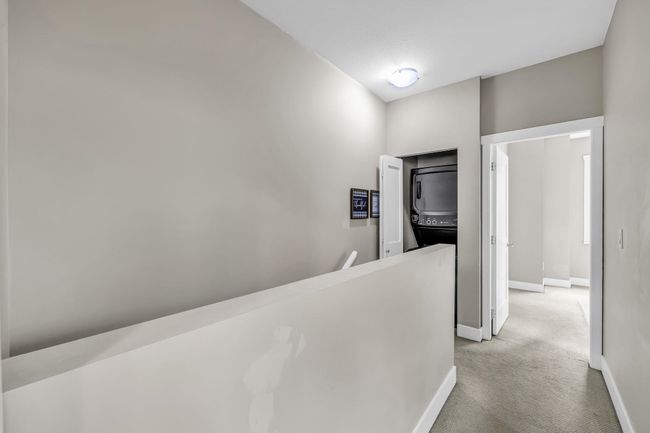 Hallway featuring stacked washer / drying machine, an upstairs landing, baseboards, and light carpet | Image 22