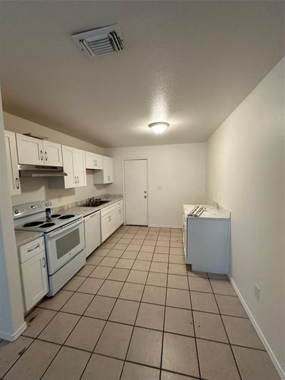 Kitchen featuring white cabinets, dishwasher, light tile patterned floors, stove, and extractor fan | Image 3