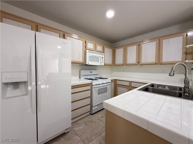 Kitchen with light brown cabinets, tile counters, white appliances, and a sink | Image 21