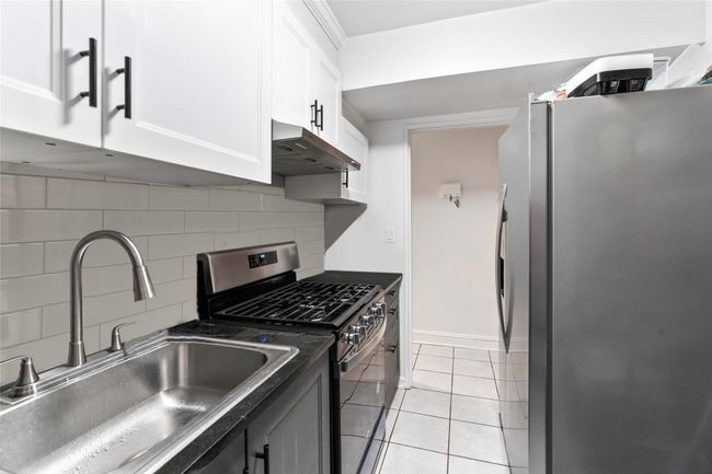 Kitchen featuring appliances with stainless steel finishes, under cabinet range hood, dark countertops, white cabinetry, and backsplash | Image 7