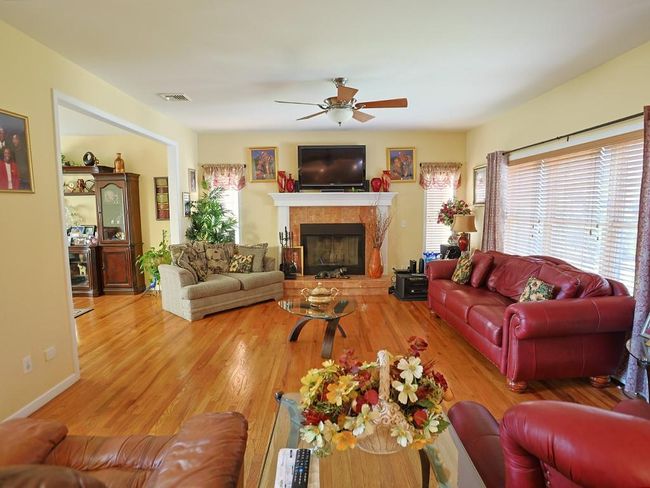 Living area featuring visible vents, wood finished floors, a fireplace, and a ceiling fan | Image 14