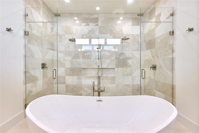 Walk-in shower with dual shower heads, finished in sleek limestone tile and marble mosaic. | Image 30