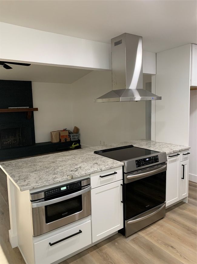 Kitchen with stove, ventilation hood, light wood finished floors, wall oven, and white cabinetry | Image 5