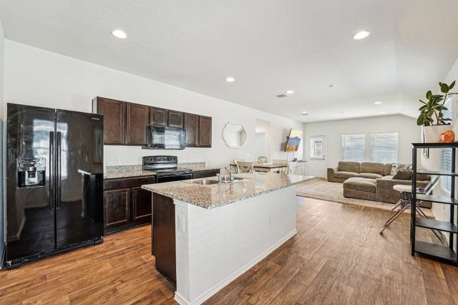 Kitchen featuring wood finished floors, a center island with sink, a sink, black appliances, and dark brown cabinetry | Image 9