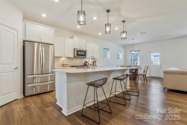 Beautiful white kitchen with quartz countertops. Sellers added the pendent lights over the island. LG fridge will come with your new home. | Image 5