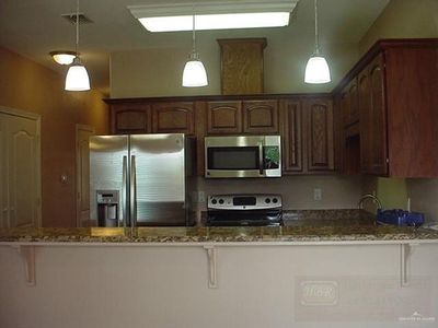 Kitchen with hanging light fixtures, dark stone countertops, and stainless steel appliances | Image 2