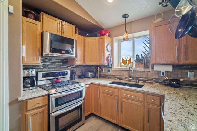 Kitchen featuring light stone countertops, stainless steel appliances, backsplash, a sink, and lofted ceiling | Image 8