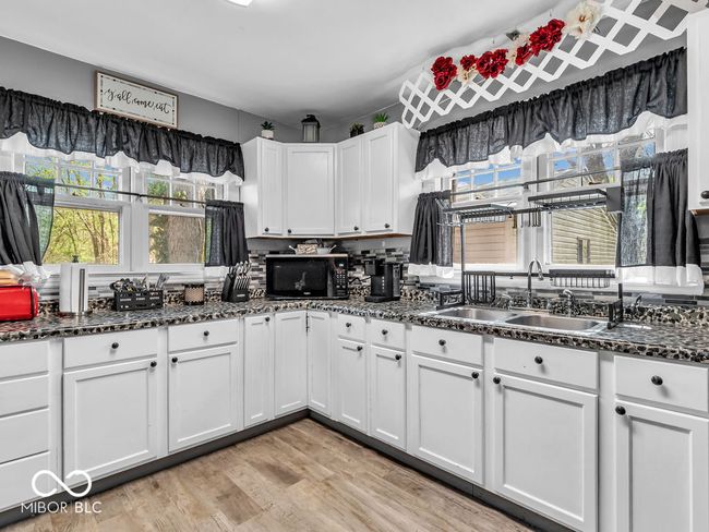 kitchen featuring dark countertops, white cabinets, vinyl plank flooring, black appliances | Image 8