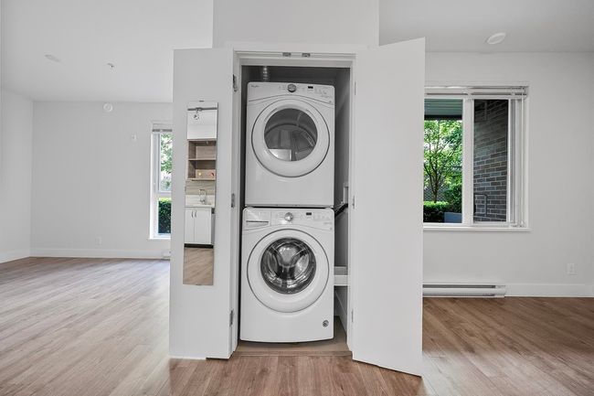 Washroom featuring stacked washer / drying machine, a baseboard heating unit, and wood finished floors | Image 24