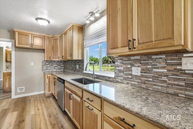 Kitchen featuring dishwasher, light wood finished floors, light stone countertops, tasteful backsplash, and light brown cabinetry | Image 20