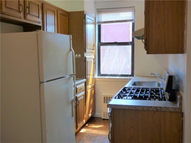 Kitchen featuring freestanding refrigerator, radiator heating unit, under cabinet range hood, brown cabinets, and a sink | Image 8