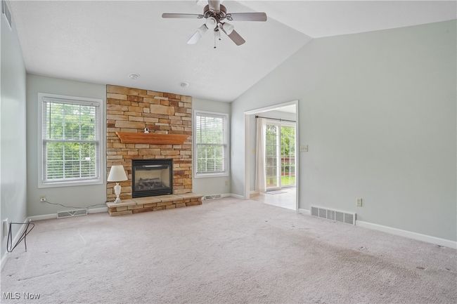 Unfurnished living room featuring plenty of natural light, a stone fireplace, vaulted ceiling, and baseboards | Image 13