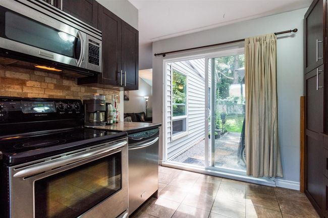 Kitchen with stainless steel appliances, decorative backsplash, dark brown cabinets, dark countertops, and light tile patterned floors | Image 10