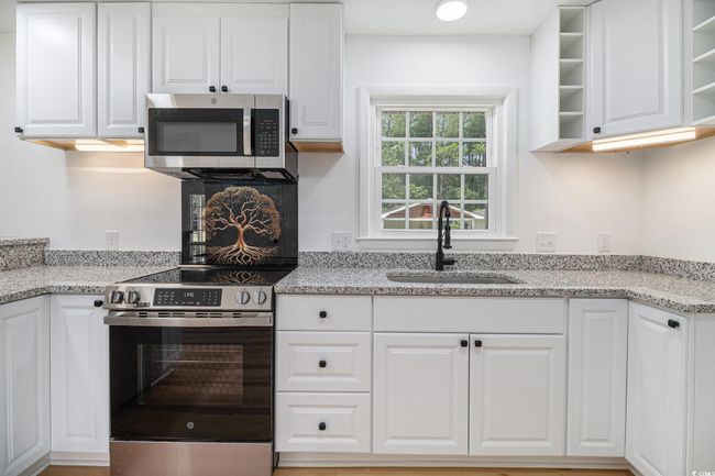 Kitchen featuring GE stainless steel appliances, white cabinetry, open shelves, stainless steel sink, stove/range back splash and granite countertops. | Image 16