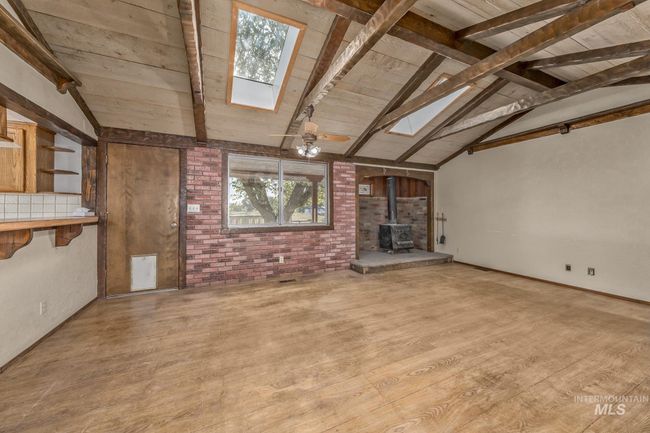 Unfurnished living room featuring a skylight, a wood stove, wood finished floors, wooden ceiling, and brick wall | Image 4