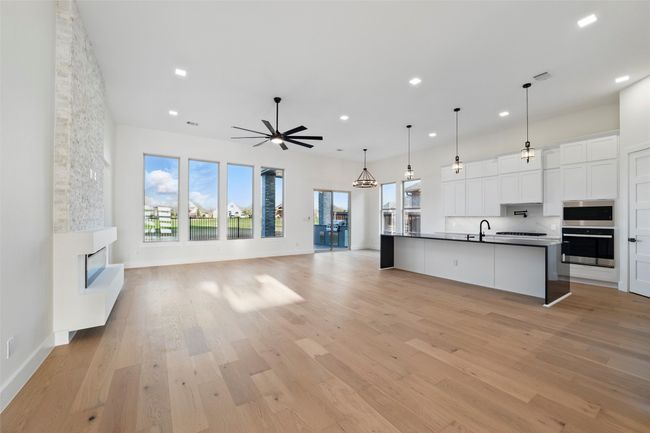 Kitchen with white cabinets, dark countertops, a ceiling fan, a stone fireplace, and open floor plan | Image 7