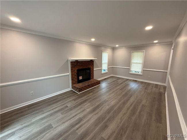 Unfurnished living room with ornamental molding, dark wood-style floors, baseboards, a brick fireplace, and recessed lighting | Image 10