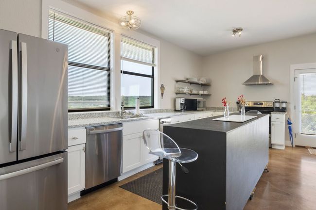 Kitchen featuring stainless steel appliances, wall chimney range hood, a sink, open shelves, and concrete flooring | Image 11