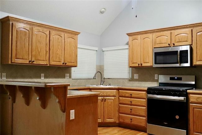 Kitchen with appliances with stainless steel finishes, tasteful backsplash, a kitchen bar, light wood-type flooring, and high vaulted ceiling | Image 7