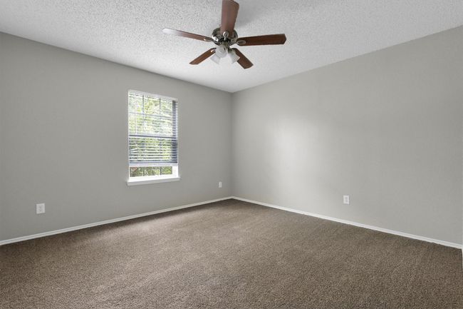 Empty room with a ceiling fan, dark carpet, a textured ceiling, and baseboards | Image 27