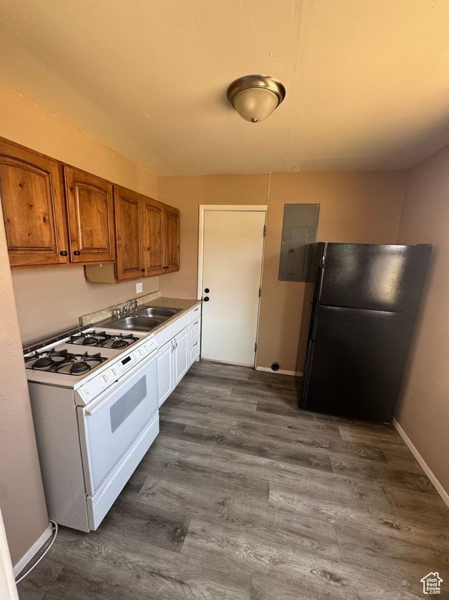 Kitchen with white gas range oven, freestanding refrigerator, electric panel, brown cabinetry, and dark wood finished floors | Image 8