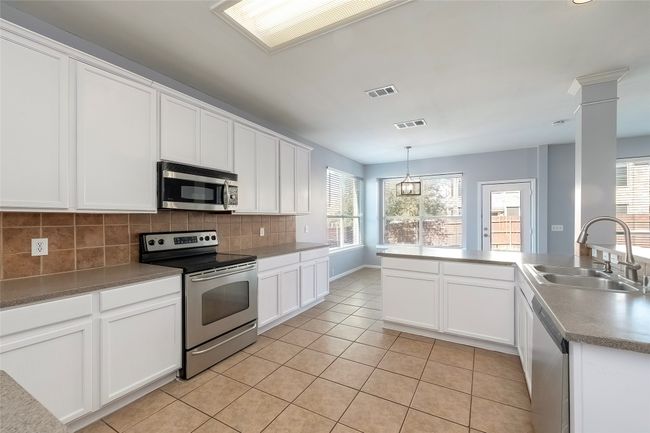 Kitchen featuring light tile patterned floors, stainless steel appliances, decorative backsplash, white cabinets, and a sink | Image 23