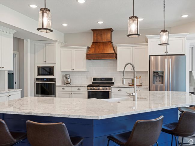 Kitchen with appliances with stainless steel finishes, premium range hood, white cabinets, tasteful backsplash, and a breakfast bar | Image 9