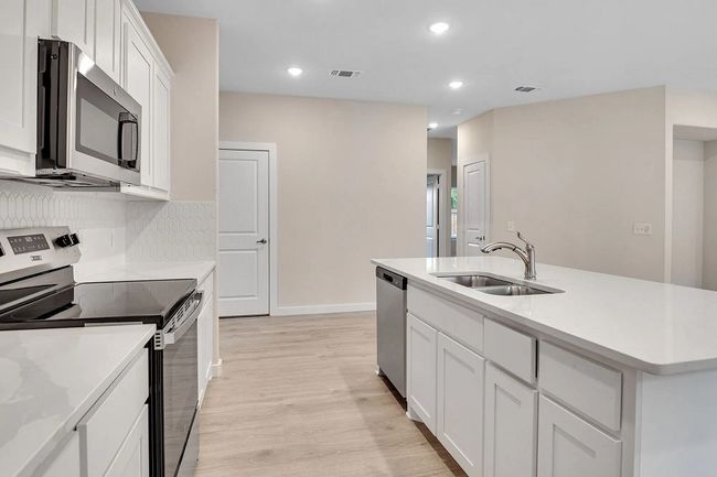Kitchen featuring appliances with stainless steel finishes, light wood-type flooring, white cabinets, light countertops, and an island with sink | Image 5