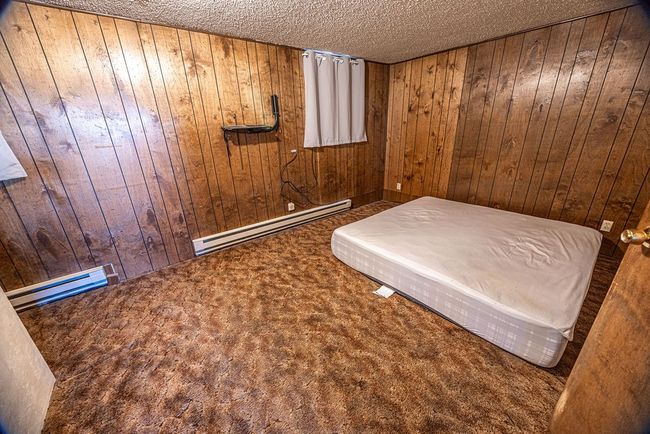 Unfurnished bedroom featuring wood walls, dark colored carpet, a textured ceiling, and a baseboard heating unit | Image 39