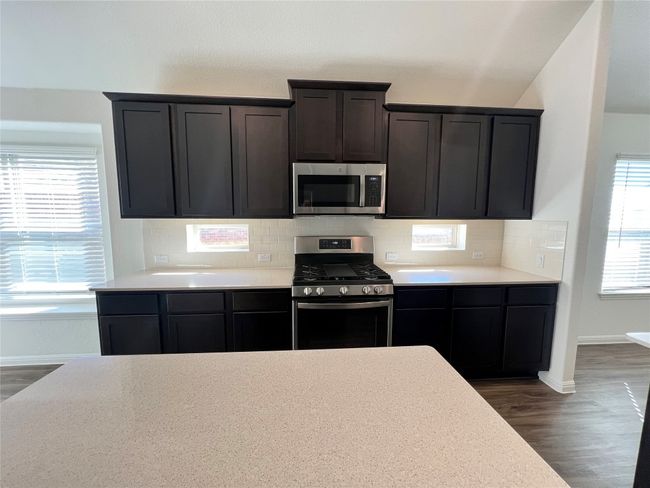 Kitchen with dark wood finished floors, stainless steel appliances, tasteful backsplash, and light stone counters | Image 10