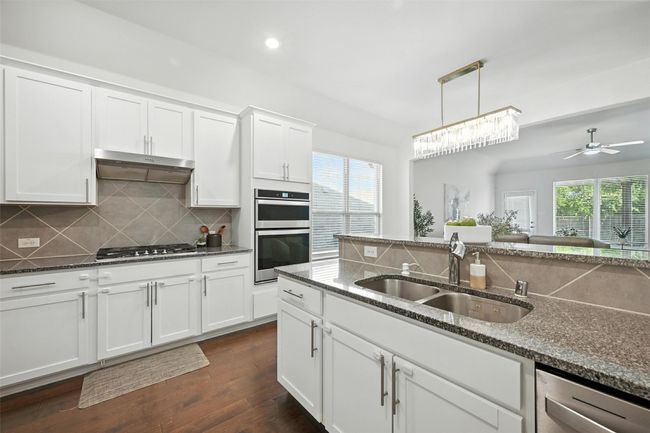 Kitchen with backsplash, dark wood finished floors, dark stone counters, white cabinetry, and ceiling fan | Image 9