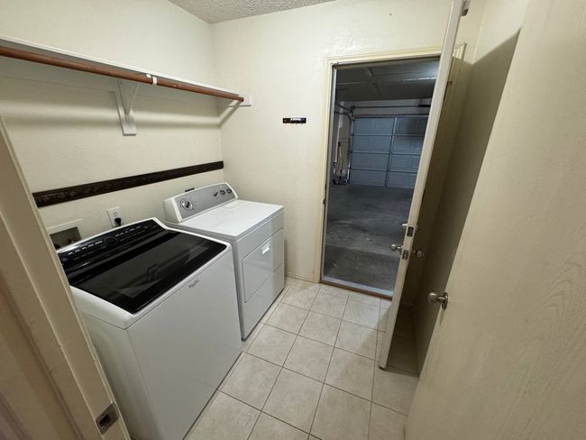 Laundry area with separate washer and dryer, light tile patterned floors, and a textured ceiling | Image 9