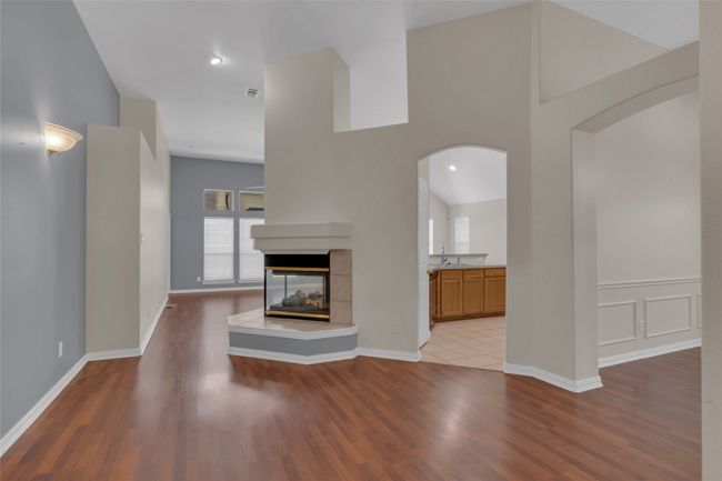 Unfurnished living room with arched walkways, wood finished floors, and a multi sided fireplace | Image 14