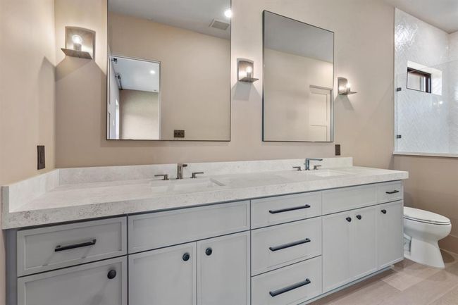 The downstairs guest suite offers a luxurious sanctuary for family and friends. With a large dual basin vanity, this doesn't feel like a secondary bath at all! Kohler plumbing fixtures in an elegant titanium sheen are repeated at the sinks and in the shower. Framed mirrors are flanked by handsome sconces to create warmth in the space. | Image 24