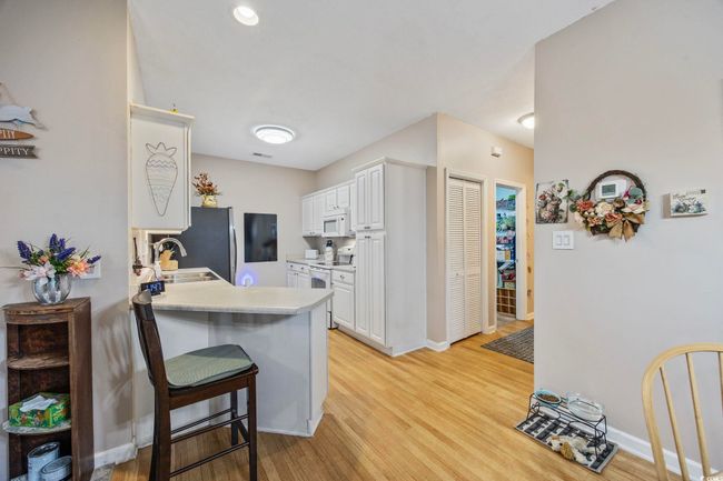Kitchen featuring white appliances, a sink, white cabinetry, a kitchen breakfast bar, and light wood-style floors | Image 11