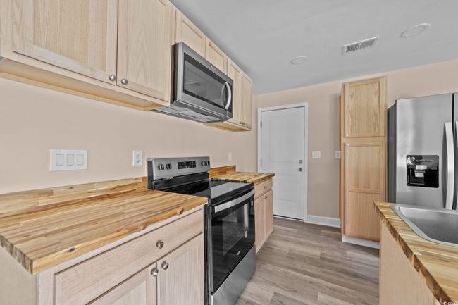 Kitchen with butcher block countertops, light brown cabinetry, stainless steel appliances, and light wood finished floors | Image 21