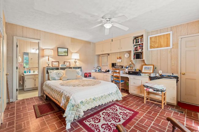 Bedroom with brick flooring, wooden walls, an office area, a ceiling fan, and ensuite bath | Image 6