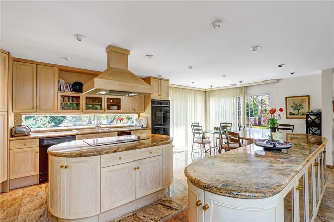 Kitchen with light stone countertops, a kitchen island, black appliances, island exhaust hood, and a sink | Image 10