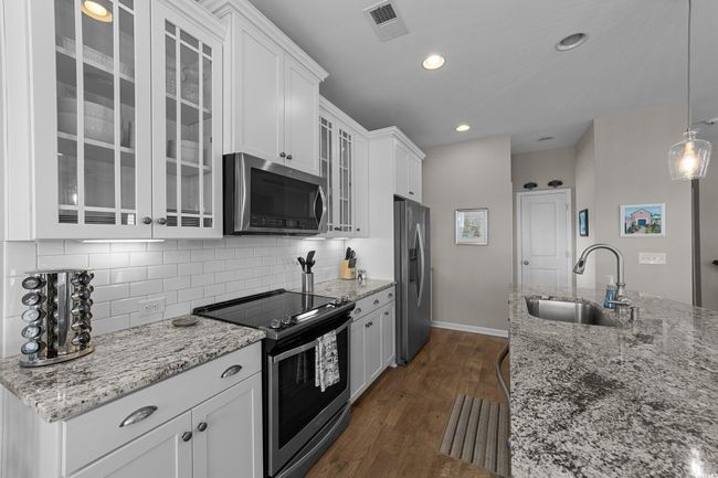 Kitchen featuring appliances with stainless steel finishes, a sink, white cabinets, dark wood-style floors, and decorative backsplash | Image 4