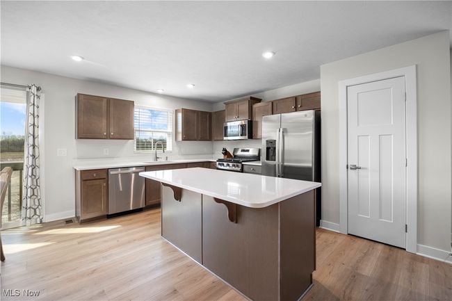 Kitchen with light wood-style flooring, a center island, a sink, light countertops, and stainless steel appliances | Image 17