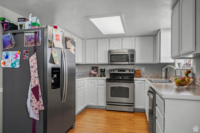 Kitchen with stainless steel appliances, light countertops, light wood finished floors, and white cabinets | Image 8