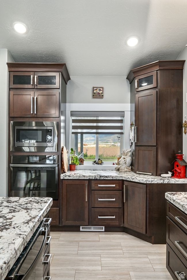 Kitchen with stainless steel appliances, dark brown cabinetry, and light stone counters | Image 29